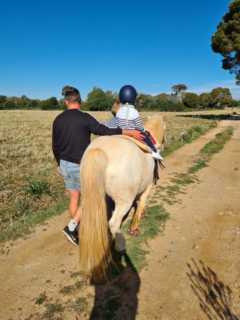 Vater begleitet sein Kind auf einem geführten Ponyausritt